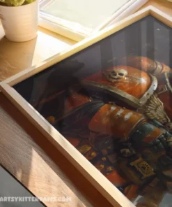 Framed warrior artwork with vibrant orange armor on a wooden table, illuminated by sunlight.